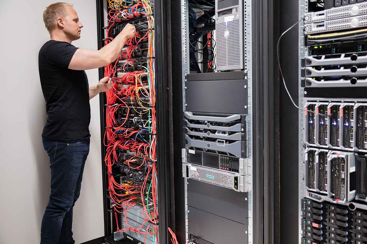 An IT field service technician attentively examining a bundle of network cables plugged into a row of server racks.