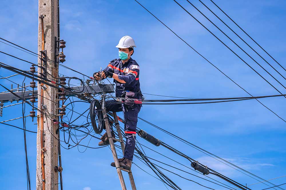 A technician balanced on a wooden ladder, diligently installing an internet cable line on an electric pole, set against a clear blue sky