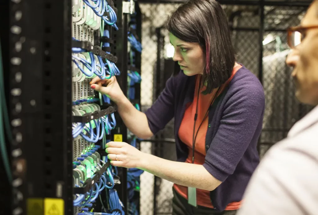 Caucasian woman and man technicians working on CAT 5 cables in a large computer server farm.